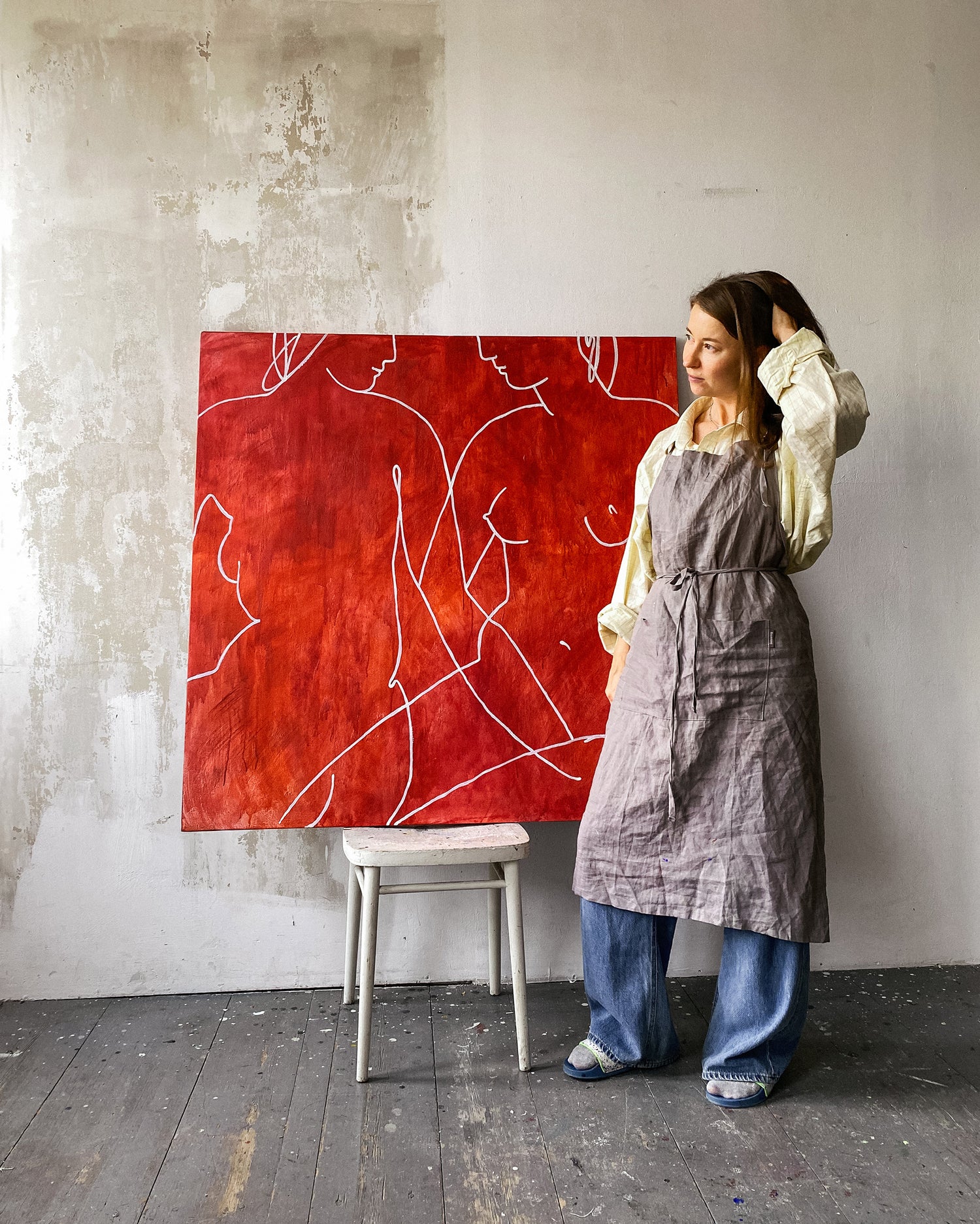 An artist Anna Pepe  standing next to a red abstract painting in an artist's studio.