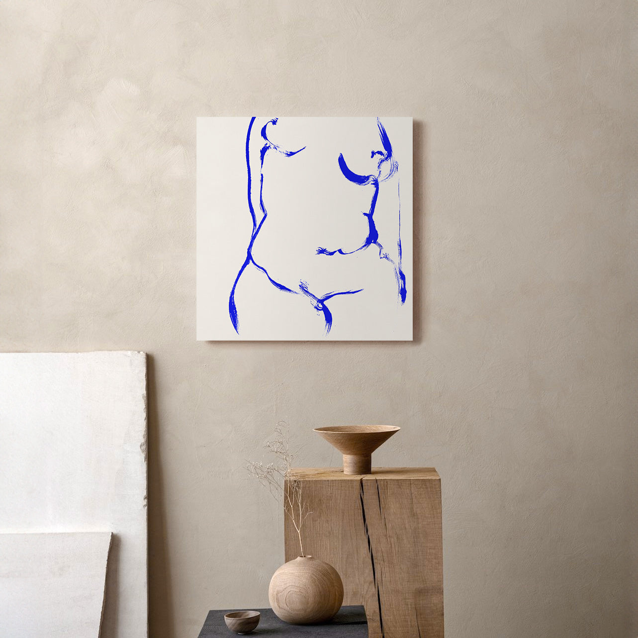 An abstract canvas print featuring a blue line drawing of a face on a white background, displayed on a textured beige wall above a wooden pedestal with neutral-toned ceramic vases. abstract painting, acrylic on canvas, contemporary collectible wall art, anna pepe, forn studio