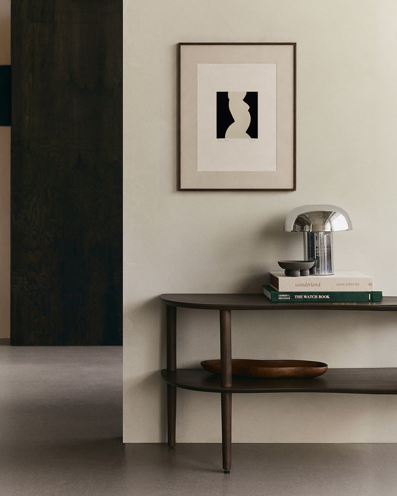 Modern interior with a dark wooden console table, books, and a lamp against a light wall with a framed abstract art piece. artist anna pepe, forn studio, abstract painting, small art work, female abstract form