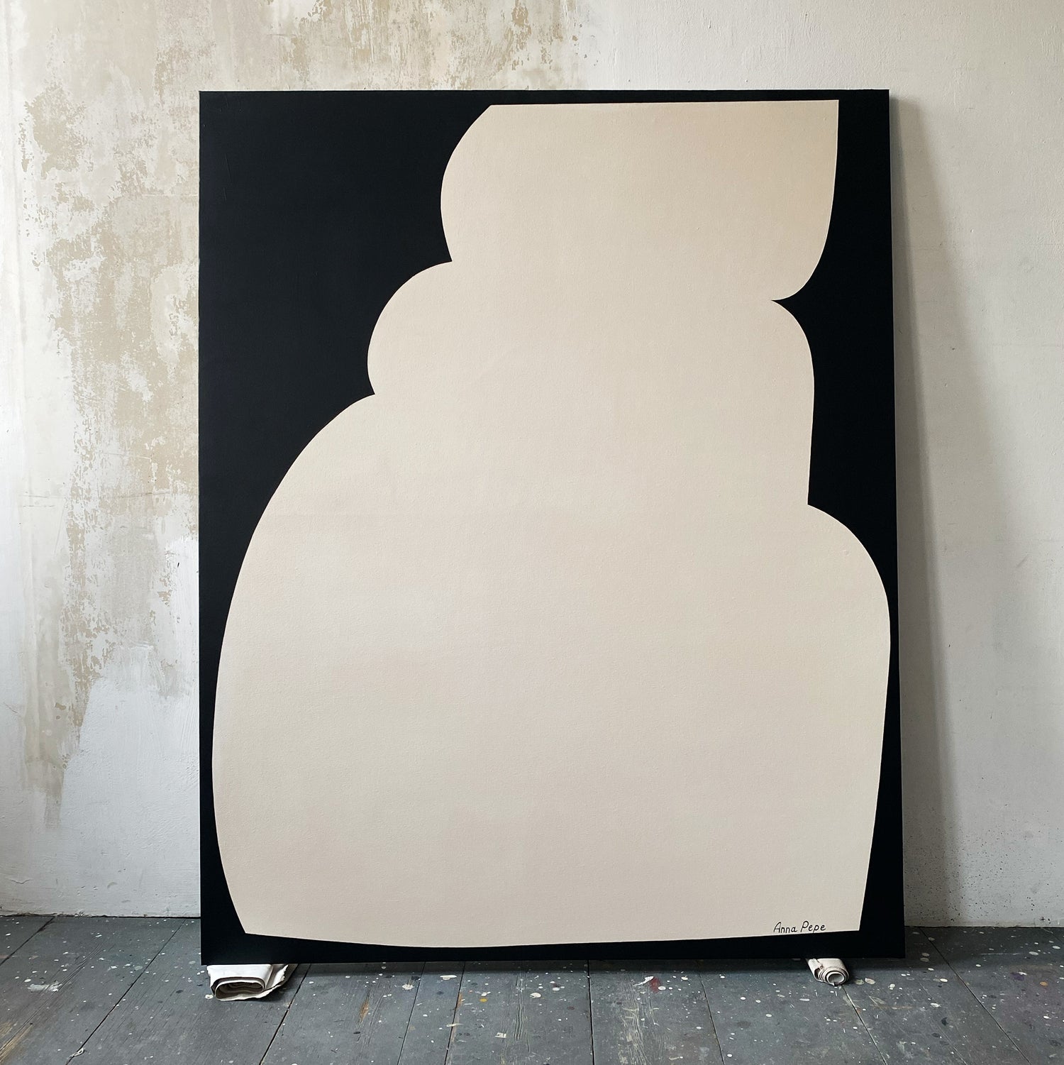 Abstract art piece with a beige shape on a black background against a textured wall.