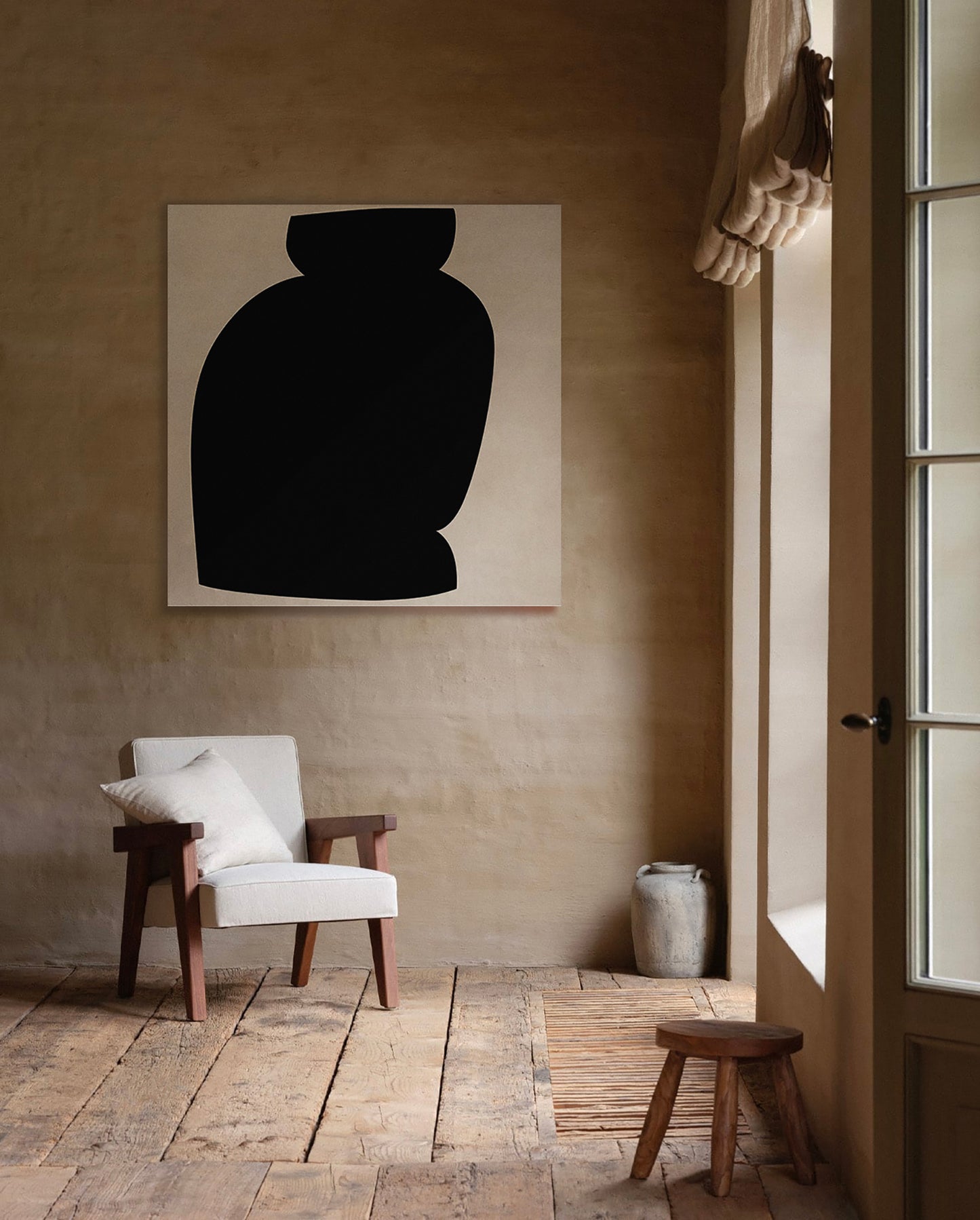 A minimalist black and white abstract canvas print of a vase hangs on a textured beige plaster wall in a rustic room with a white armchair, wooden floor, and a small stool. large canvas, acrylic on canvas, oversized wall art, abstract art, Anna Pepe, forn Studio