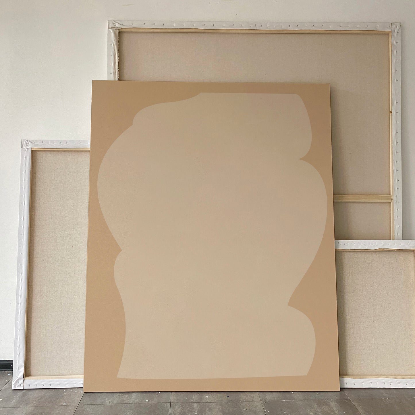 A minimalist abstract canvas painting in warm beige and tan tones, displayed leaning against other painted canvases in a studio setting. large canvas, acrylic on canvas, oversized wall art, abstract art, Anna Pepe, forn Studio