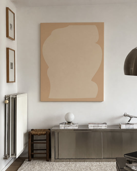 A large abstract canvas print with two beige shapes hangs on a white wall above a metallic console table in a modern, minimalist room. large canvas, acrylic on canvas, oversized wall art, abstract art, Anna Pepe, forn Studio