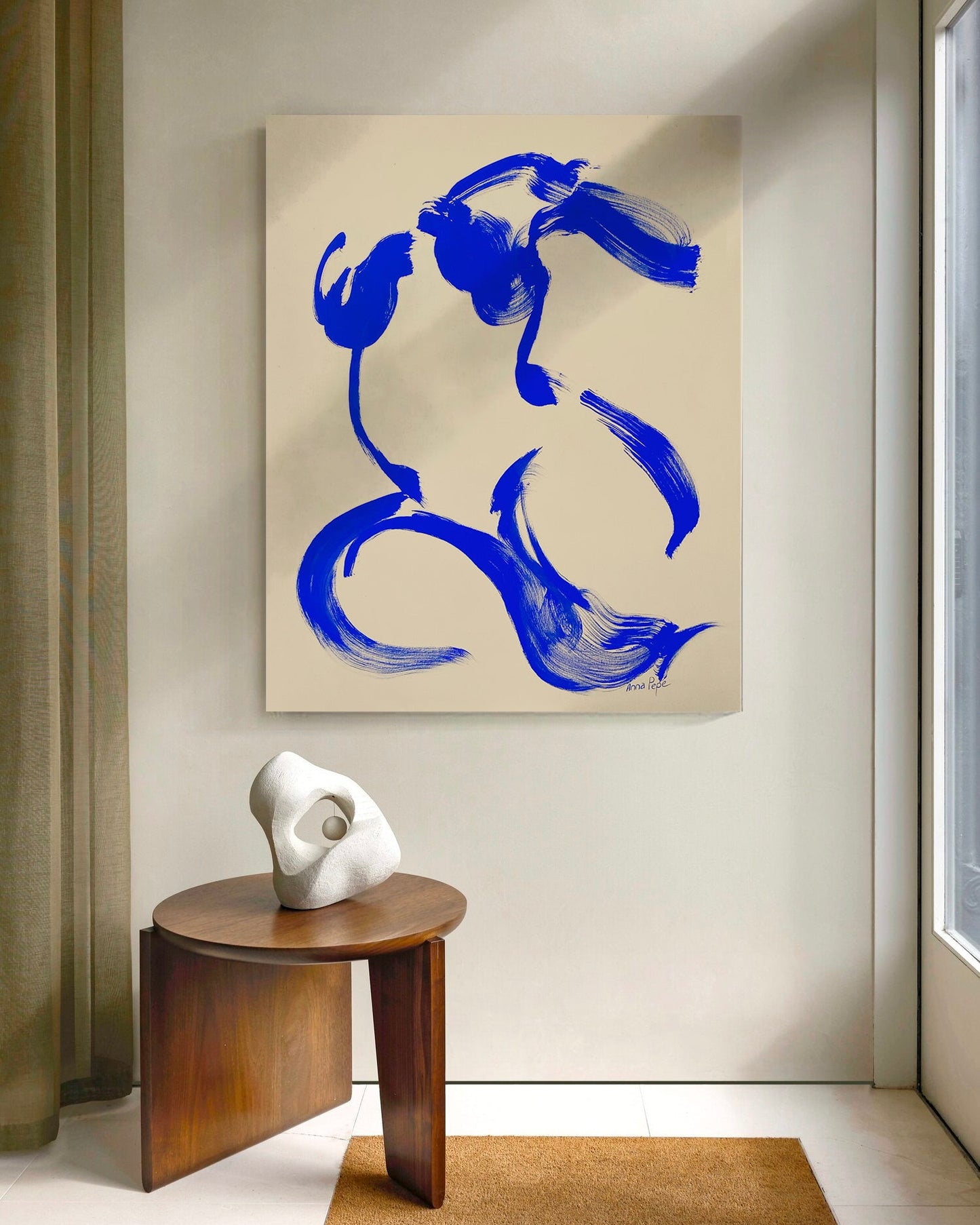 Abstract blue painting on a beige wall with a wooden side table and sculpture in a room. Artist Anna Pepe