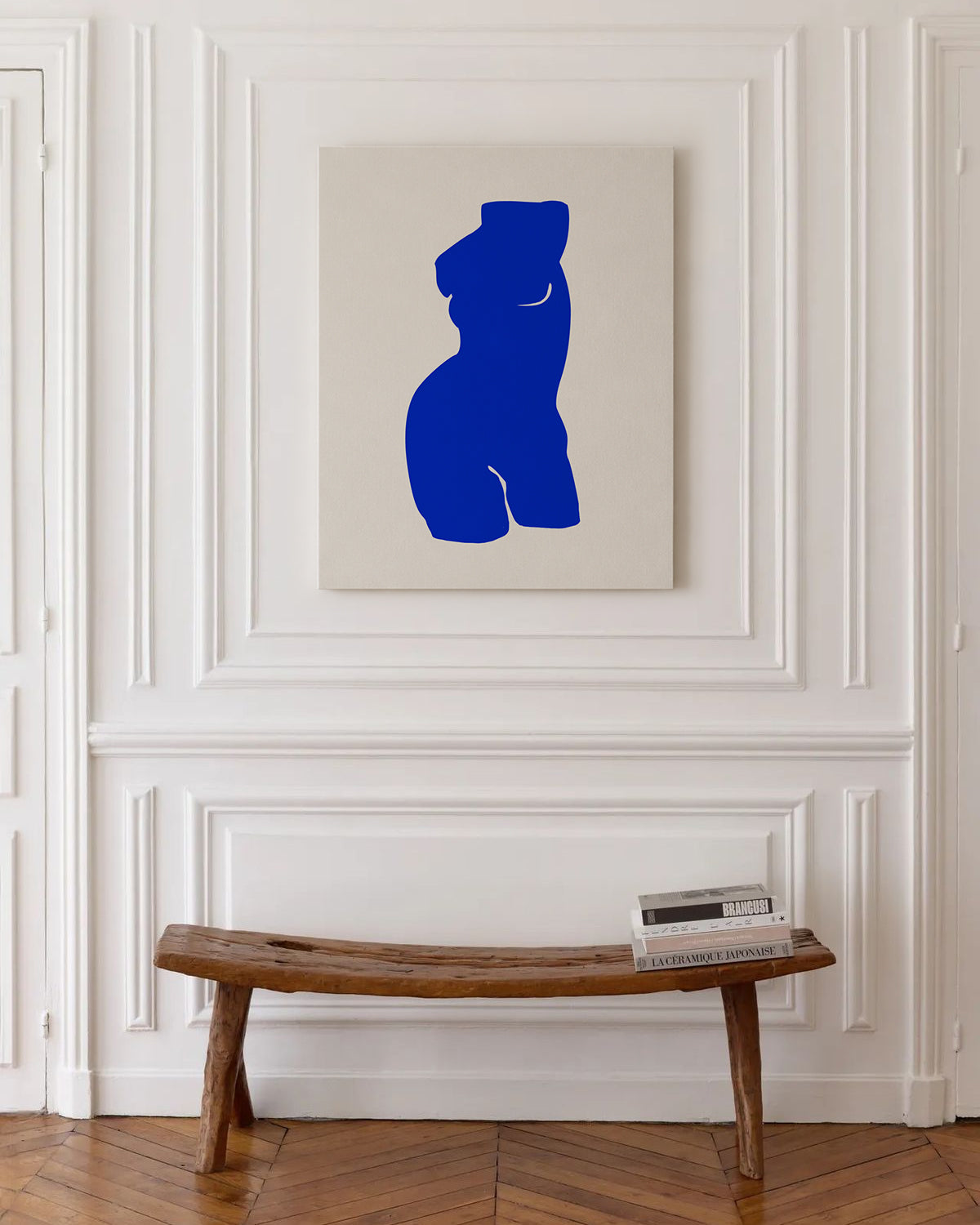 Blue abstract sculpture on a beige wall above a wooden bench.